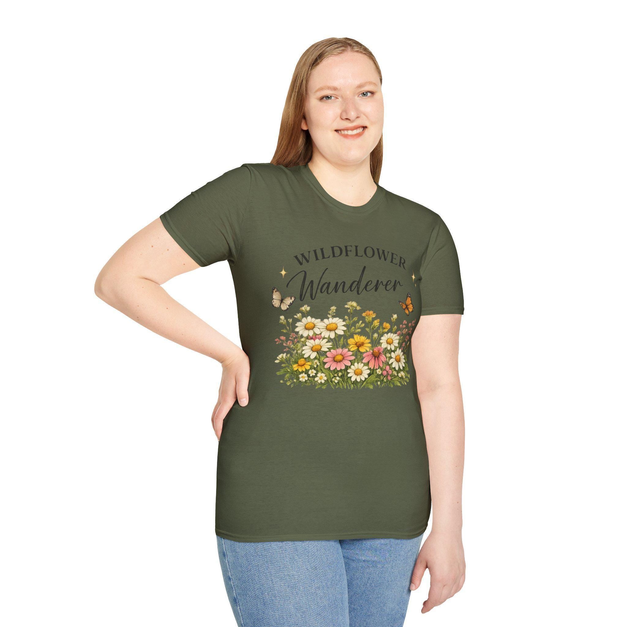 A smiling woman with long blonde hair wears a dark green t-shirt with a graphic of colorful wildflowers and butterflies, with the text "WILDFLOWER Wanderer" above.