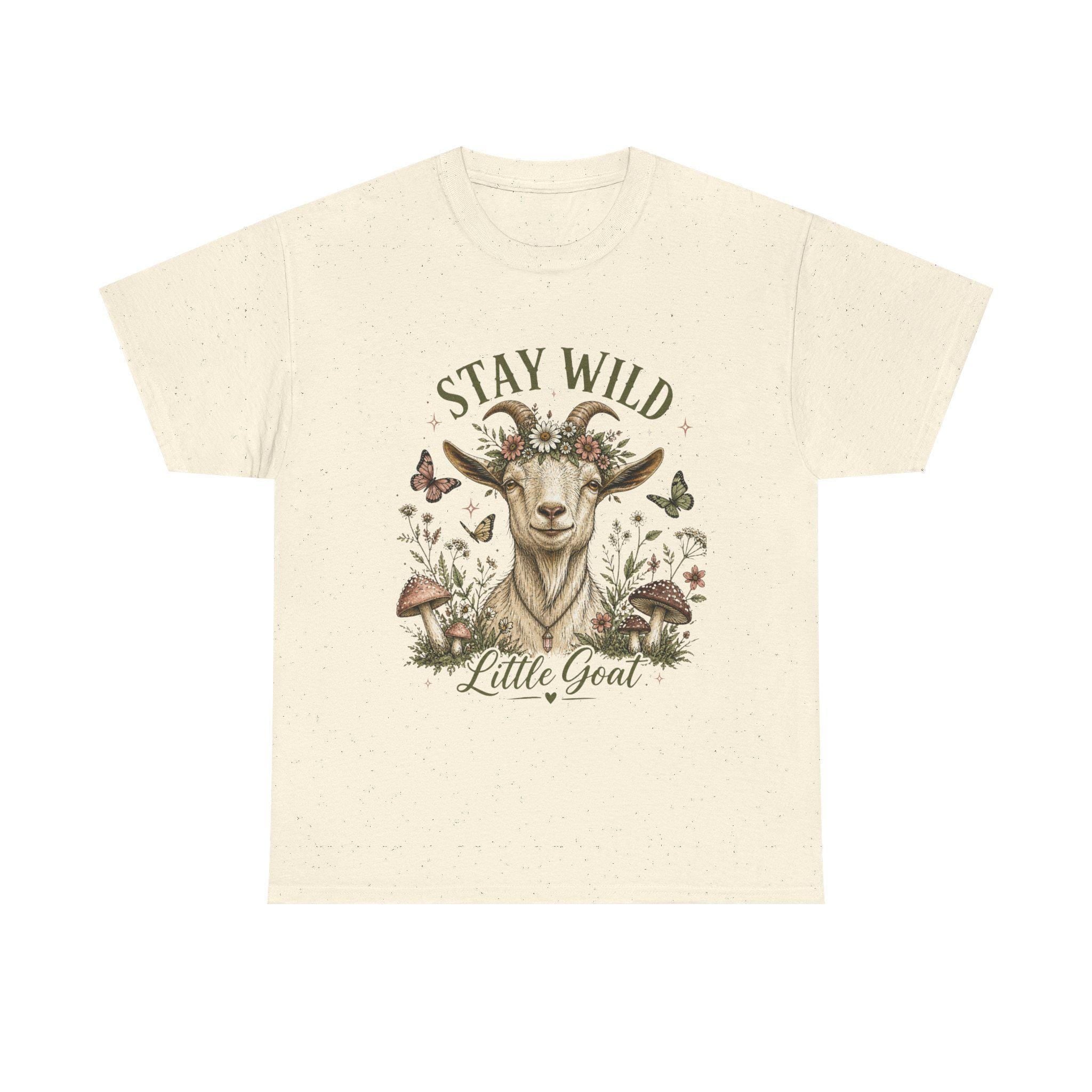 A cream t-shirt with a graphic of a goat wearing a floral crown, surrounded by mushrooms and butterflies, with the text "Stay Wild Little Goat."