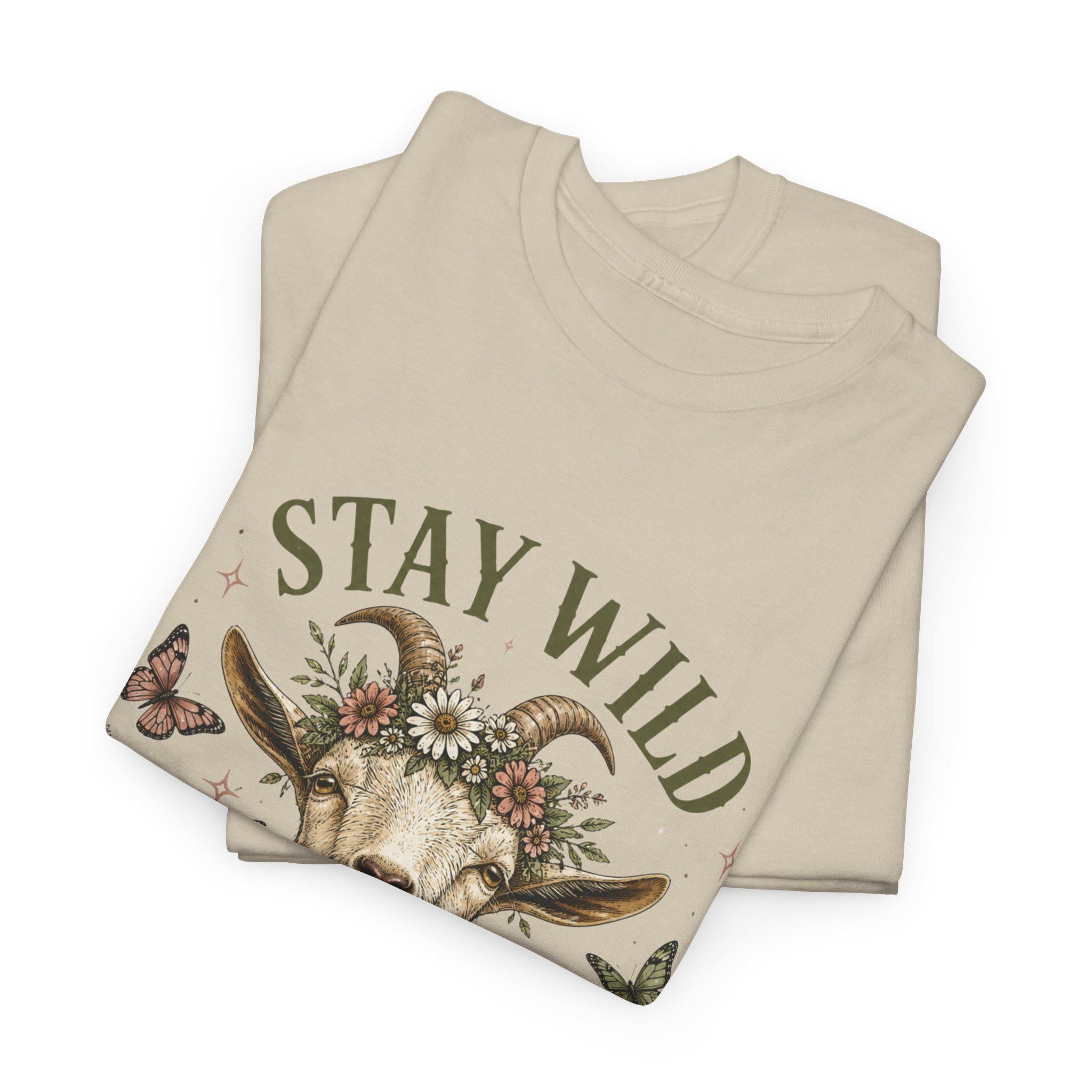 Two folded light beige t-shirts, with the top one displaying the upper half of a goat wearing a floral crown and the text "Stay Wild."