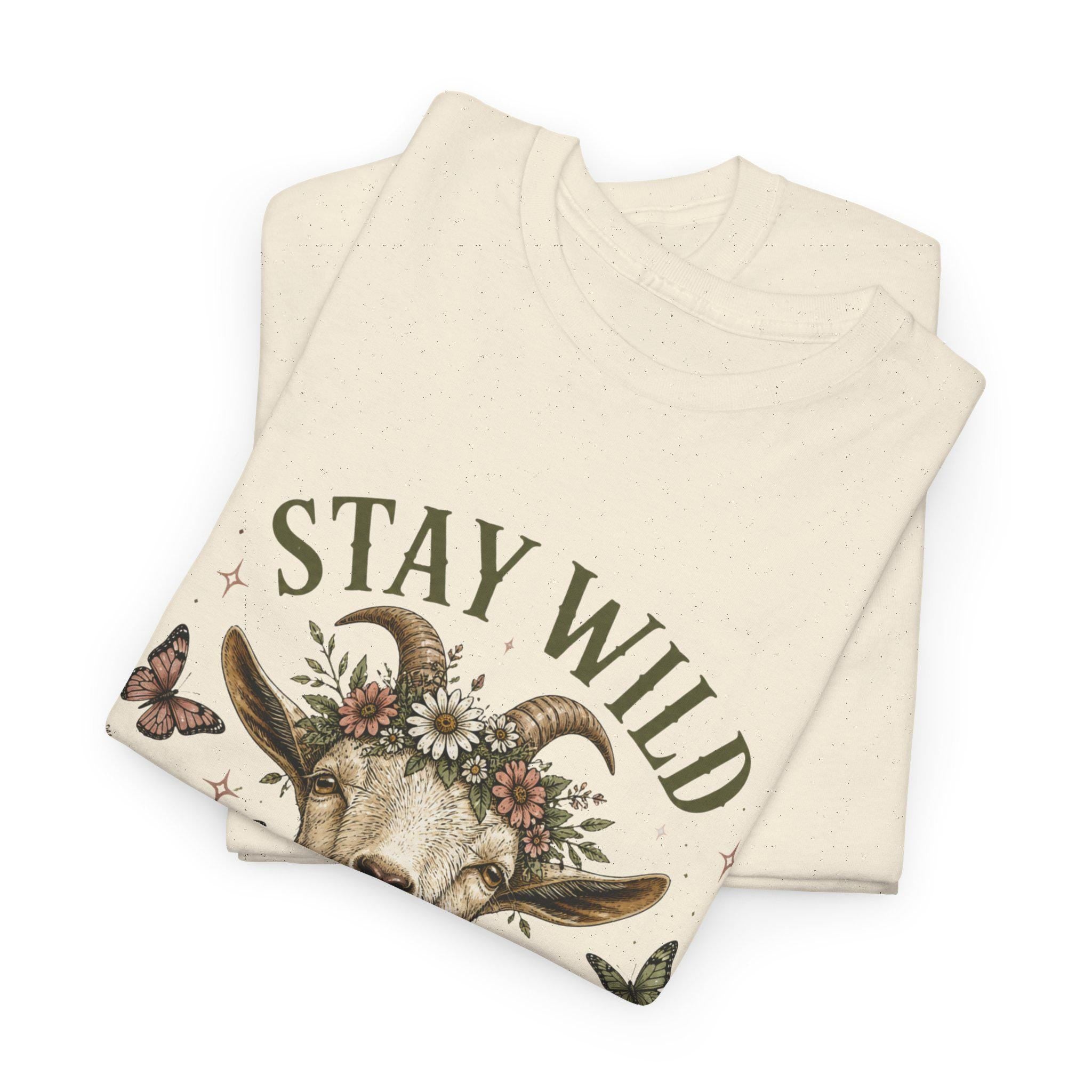 A folded cream t-shirt with a graphic of a goat's head wearing a floral crown, surrounded by the words "STAY WILD" and butterflies.