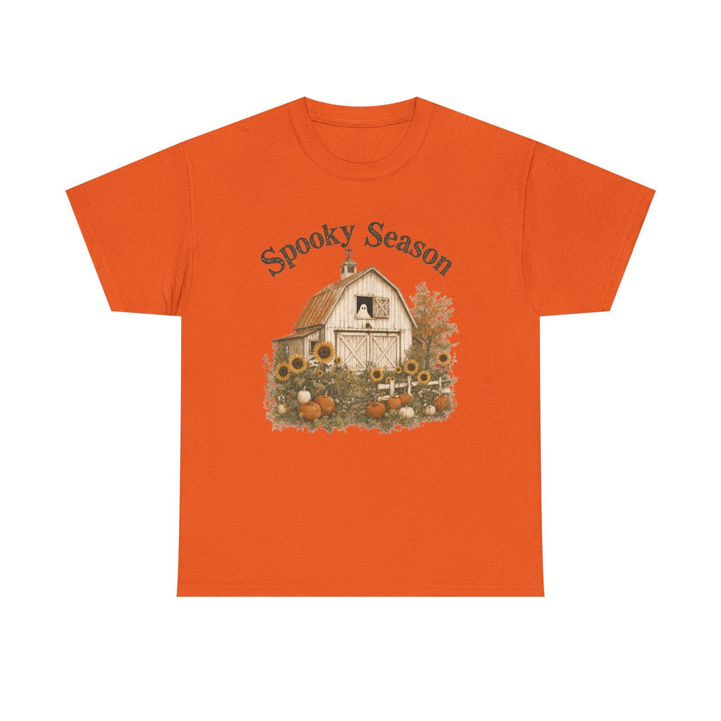 An orange t-shirt with a graphic of a barn, sunflowers, pumpkins, and a ghost in a window, with "Spooky Season" text.