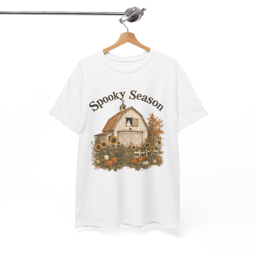 A white t-shirt hanging on a wooden hanger, displaying a graphic of a white barn, sunflowers, and pumpkins, with "Spooky Season" text above.