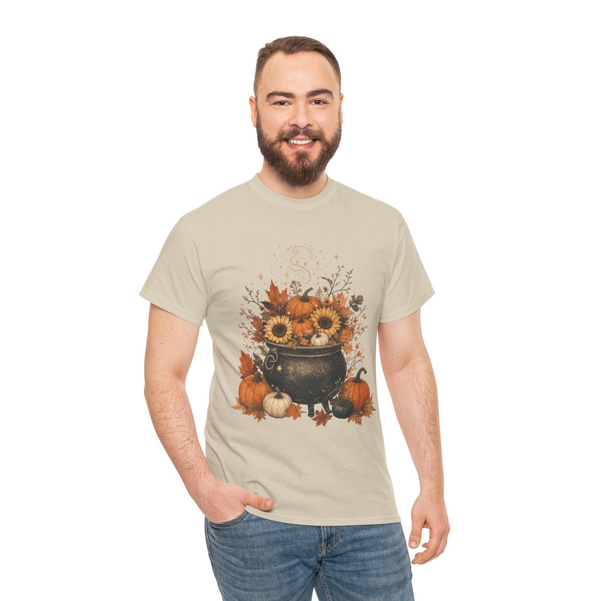 A smiling man with a beard wears a light tan short-sleeved t-shirt with a fall-themed graphic of a black cauldron filled with sunflowers, pumpkins, and autumn leaves.