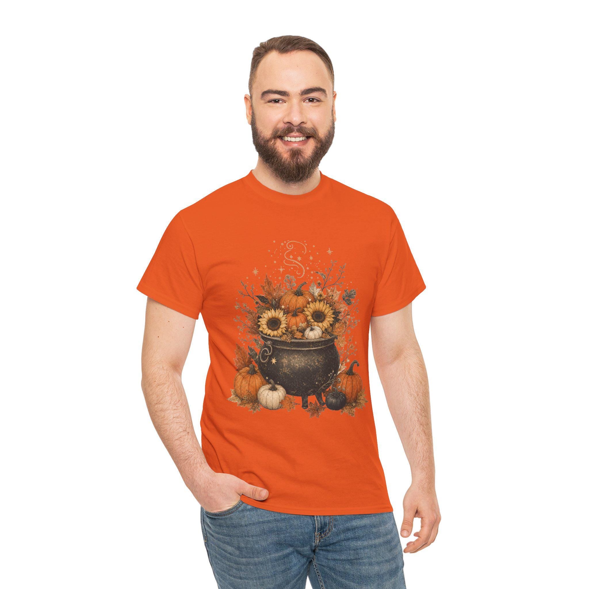 A man with a beard smiles while wearing an orange t-shirt with a graphic of a black cauldron filled with pumpkins, sunflowers, and autumn leaves.