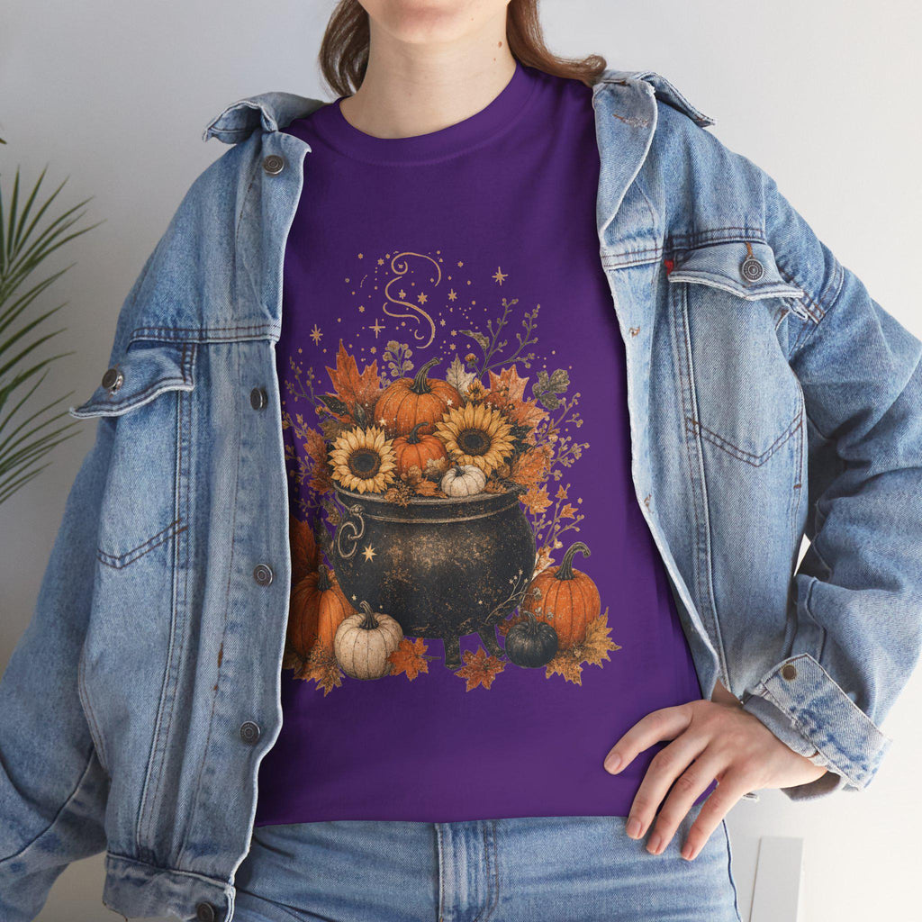 A woman in a denim jacket wears a purple t-shirt with a graphic of a black cauldron filled with pumpkins, sunflowers, and autumn leaves.