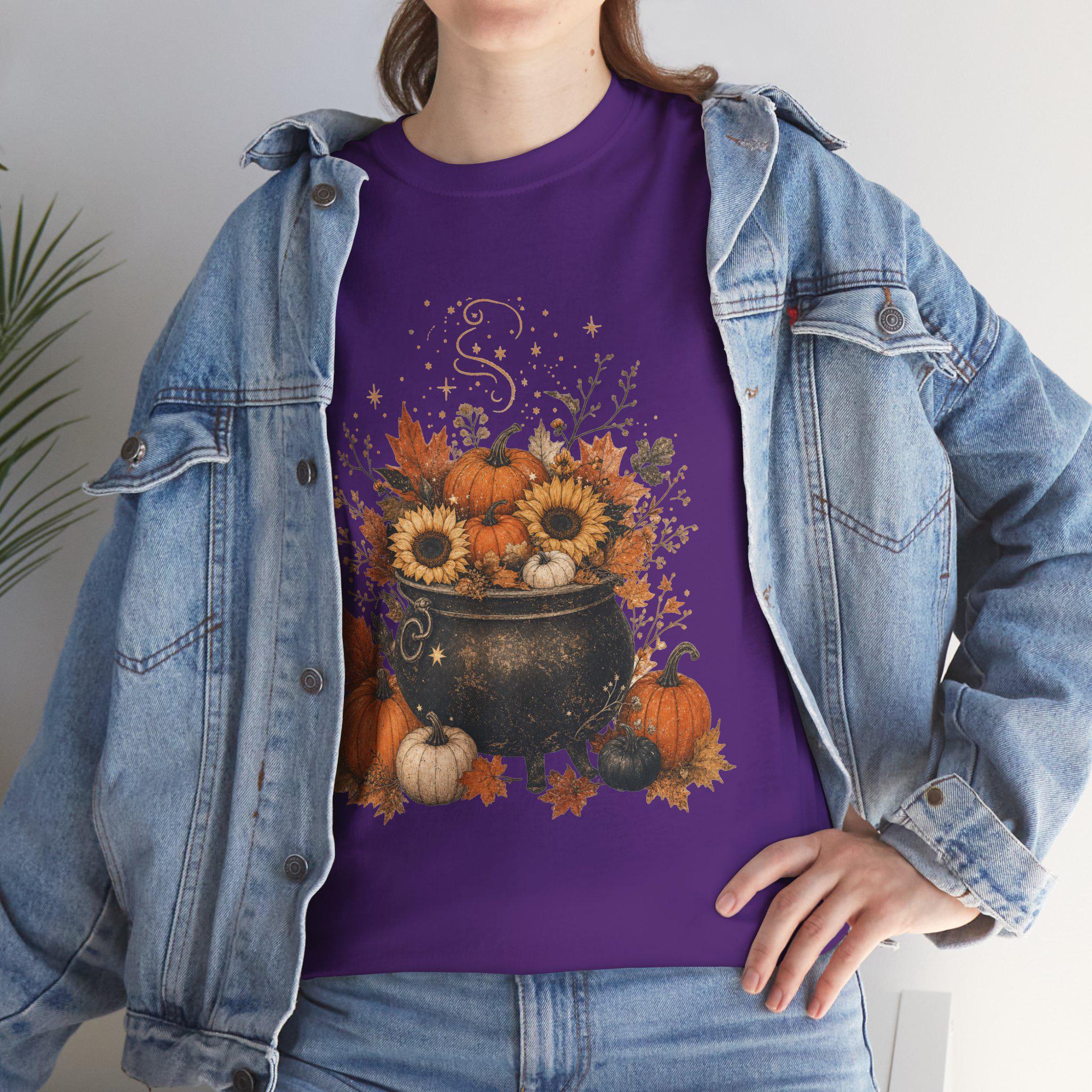 A woman in a denim jacket wears a purple t-shirt with a graphic of a black cauldron filled with pumpkins, sunflowers, and autumn leaves.