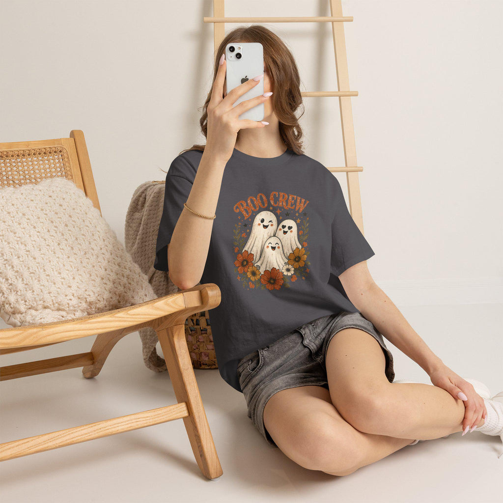 A person wearing a charcoal gray t-shirt with a "Boo Crew" graphic featuring three ghosts surrounded by orange and white flowers, sitting on a light-colored floor.