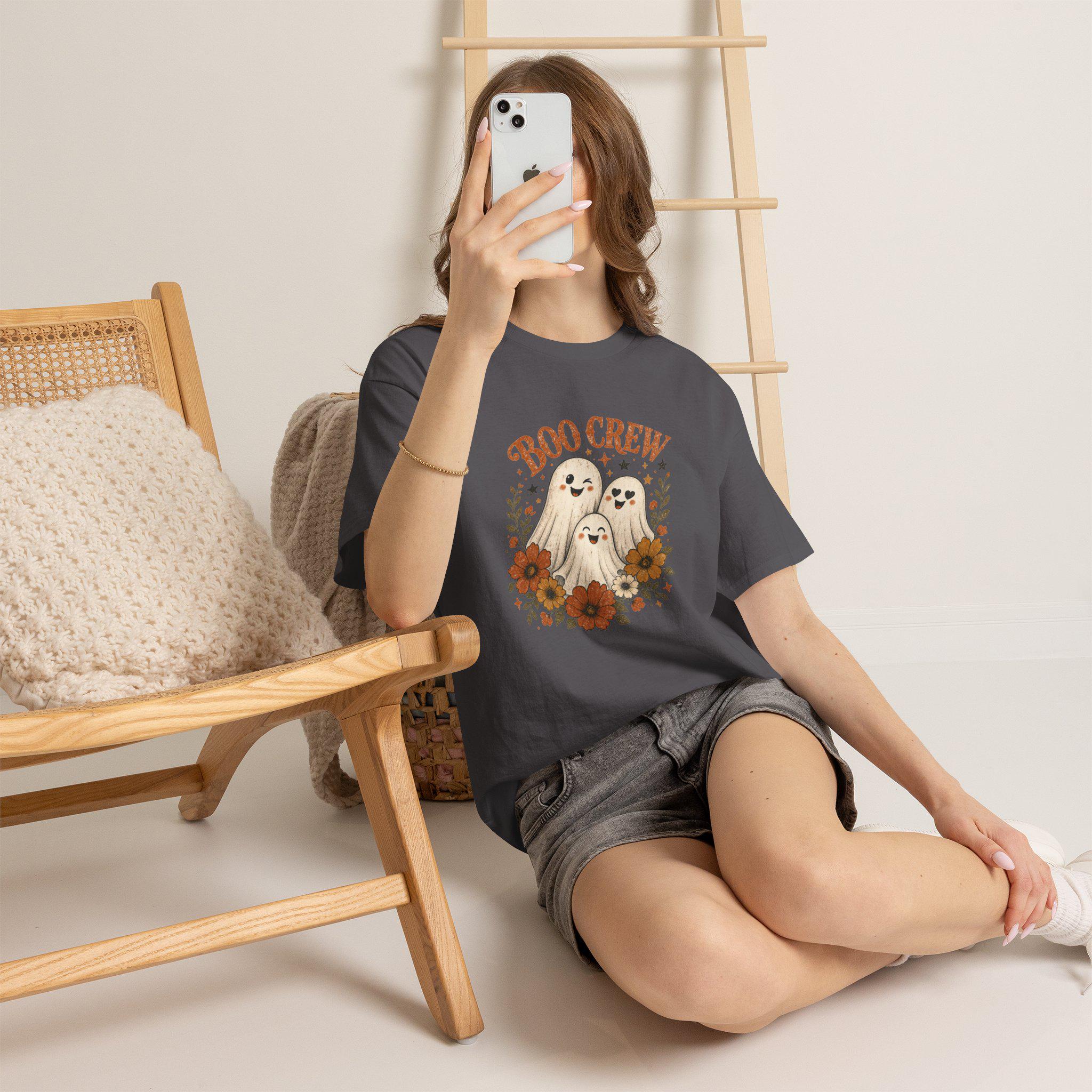 A person wearing a charcoal gray t-shirt with a "Boo Crew" graphic featuring three ghosts surrounded by orange and white flowers, sitting on a light-colored floor.