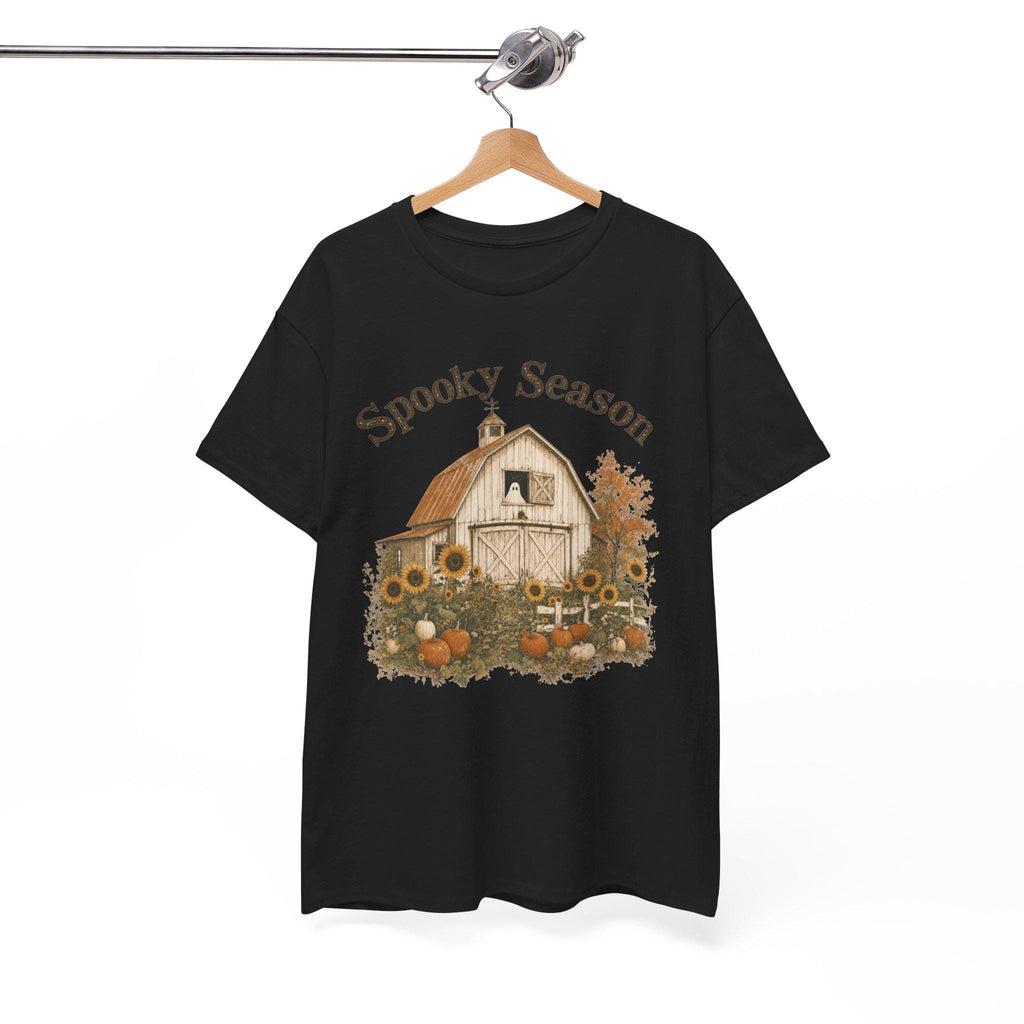 A black t-shirt hanging on a wooden hanger, displaying a graphic of a white barn, sunflowers, and pumpkins, with "Spooky Season" text above.