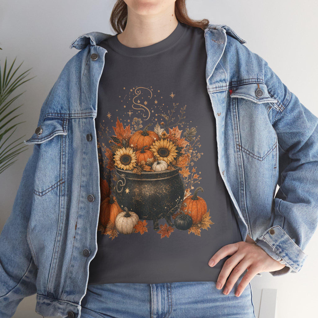 A woman in a denim jacket wears a dark gray t-shirt with a graphic of a black cauldron filled with pumpkins, sunflowers, and autumn leaves.