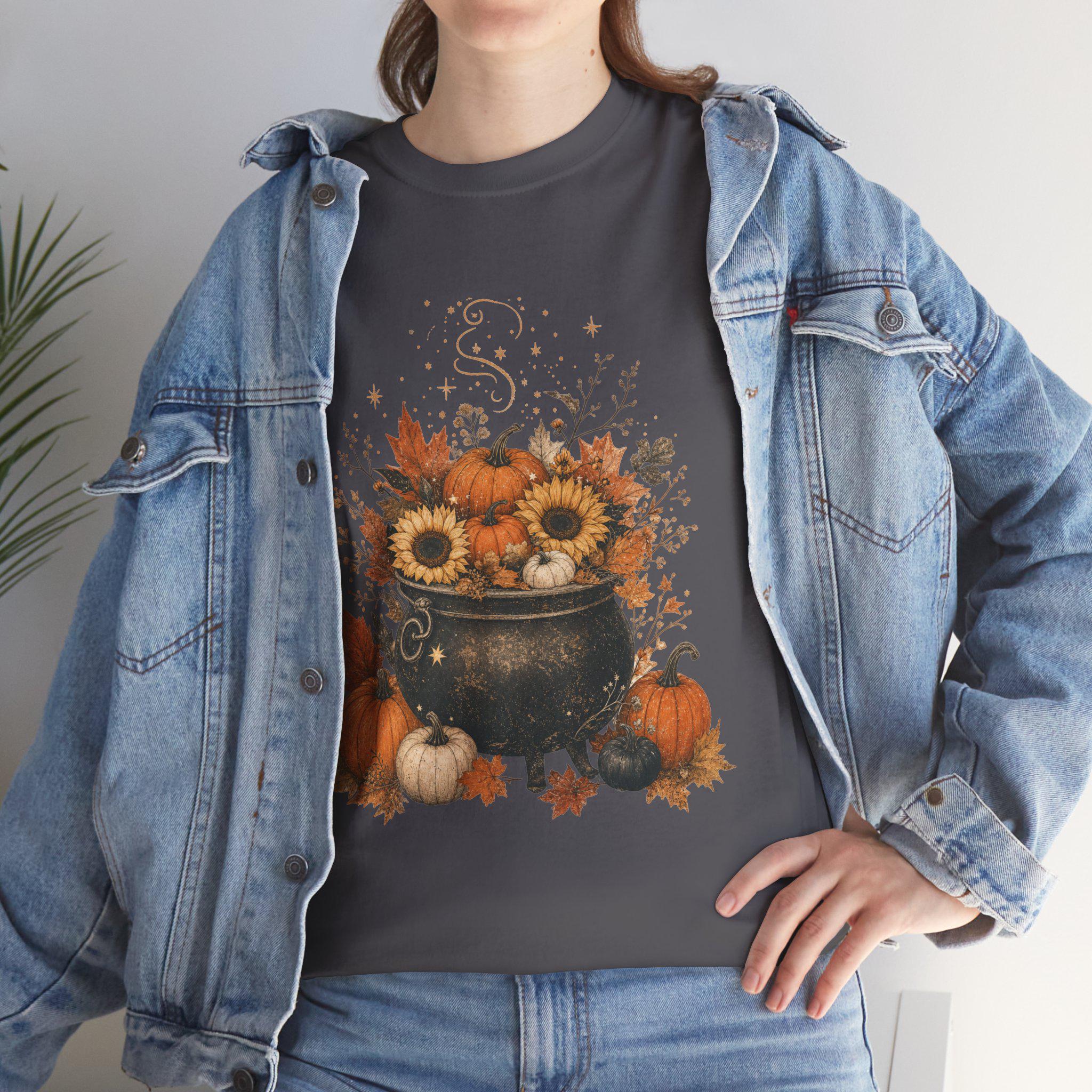 A woman in a denim jacket wears a dark gray t-shirt with a graphic of a black cauldron filled with pumpkins, sunflowers, and autumn leaves.
